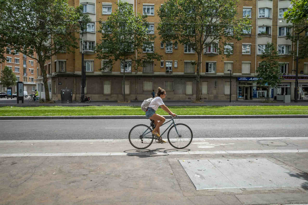 Woman cycling on an urban street bike lane beside a row of buildings.