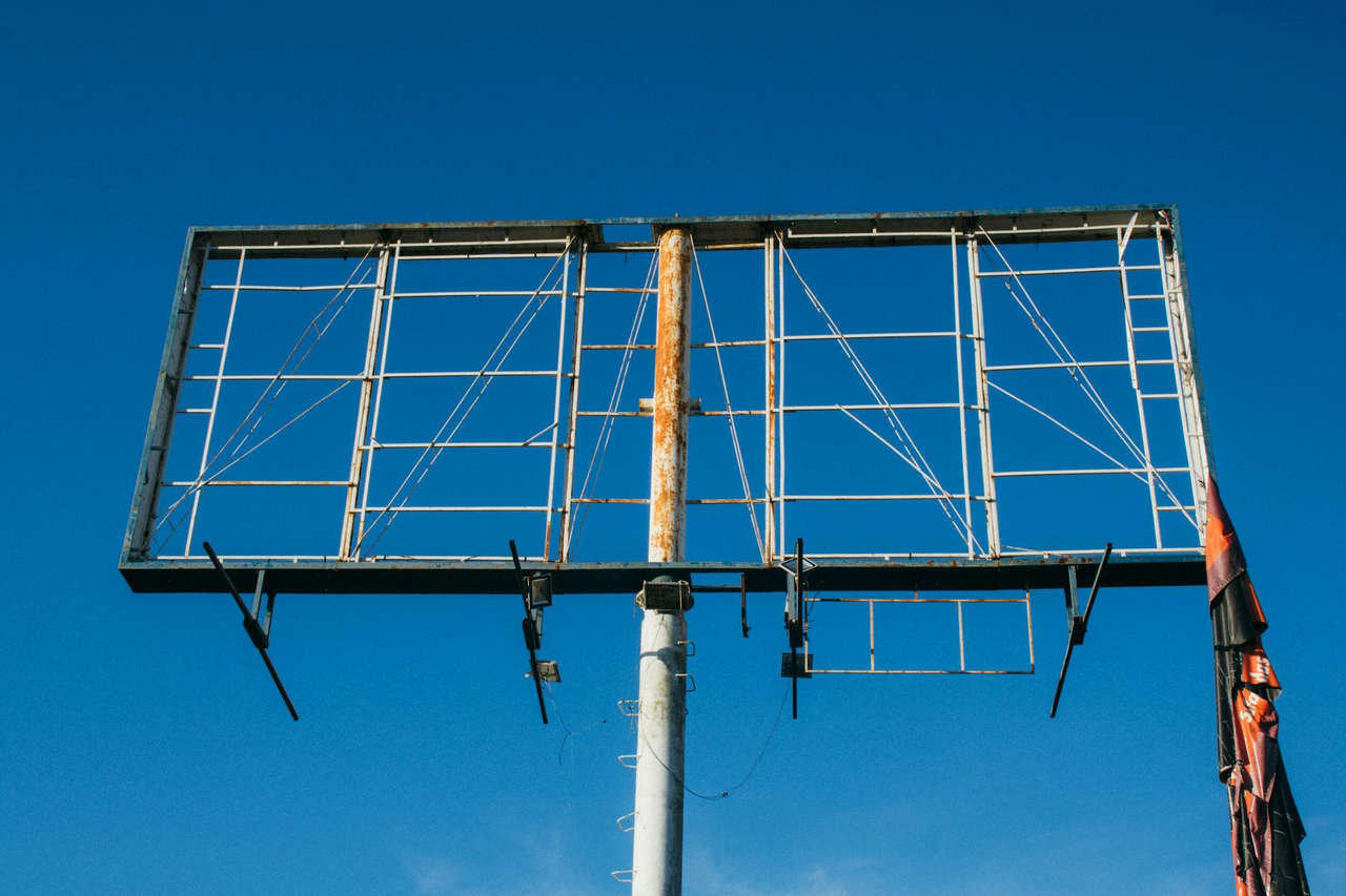 A large rusted billboard structure reaching into a clear blue sky.