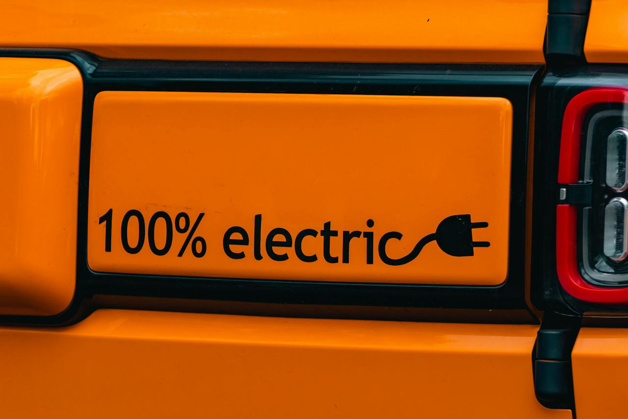 Vibrant orange electric vehicle with a '100% electric' emblem, showcasing eco-friendly transportation.