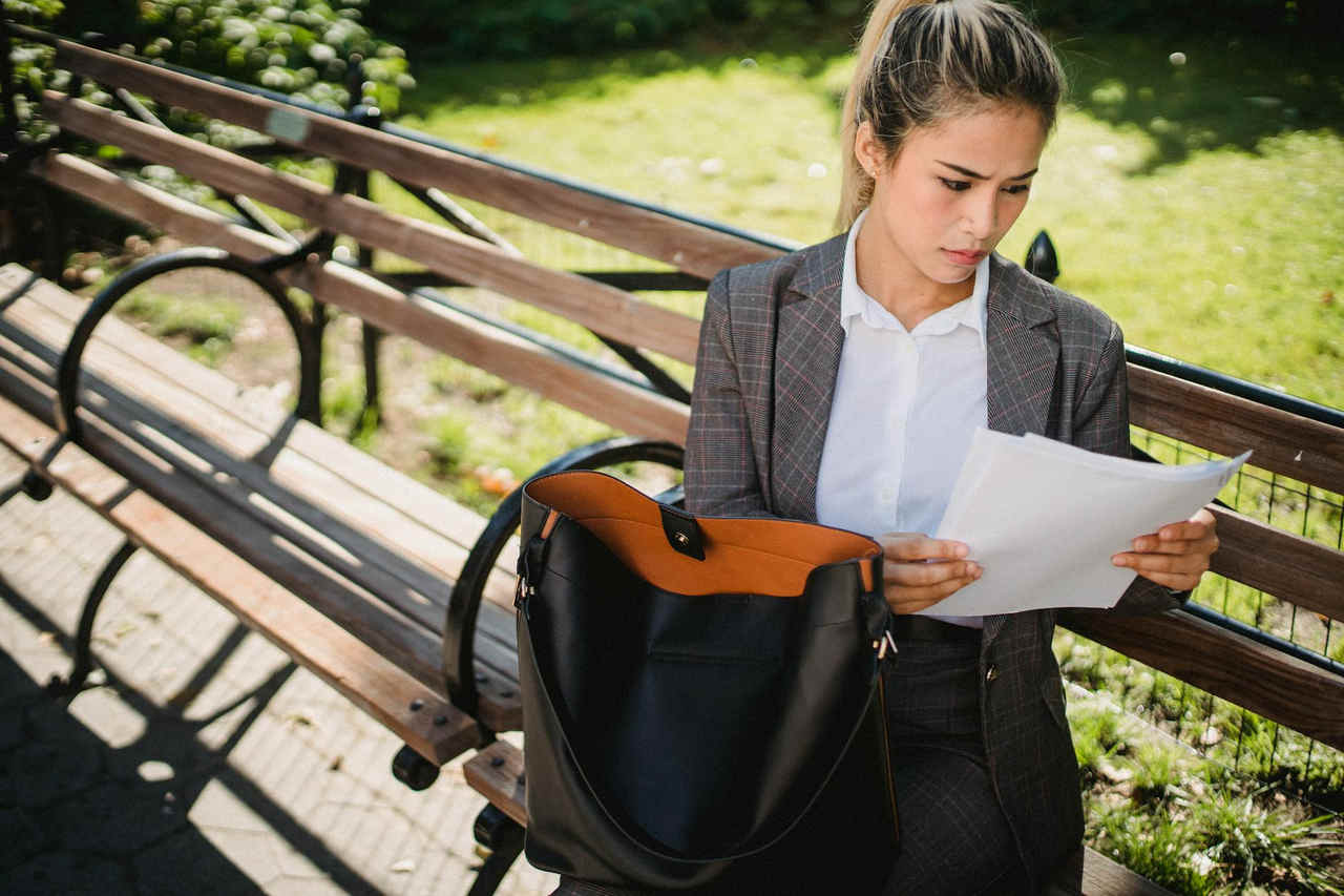 Professional woman in suit reading documents on park bench, showcasing business elegance outdoors.