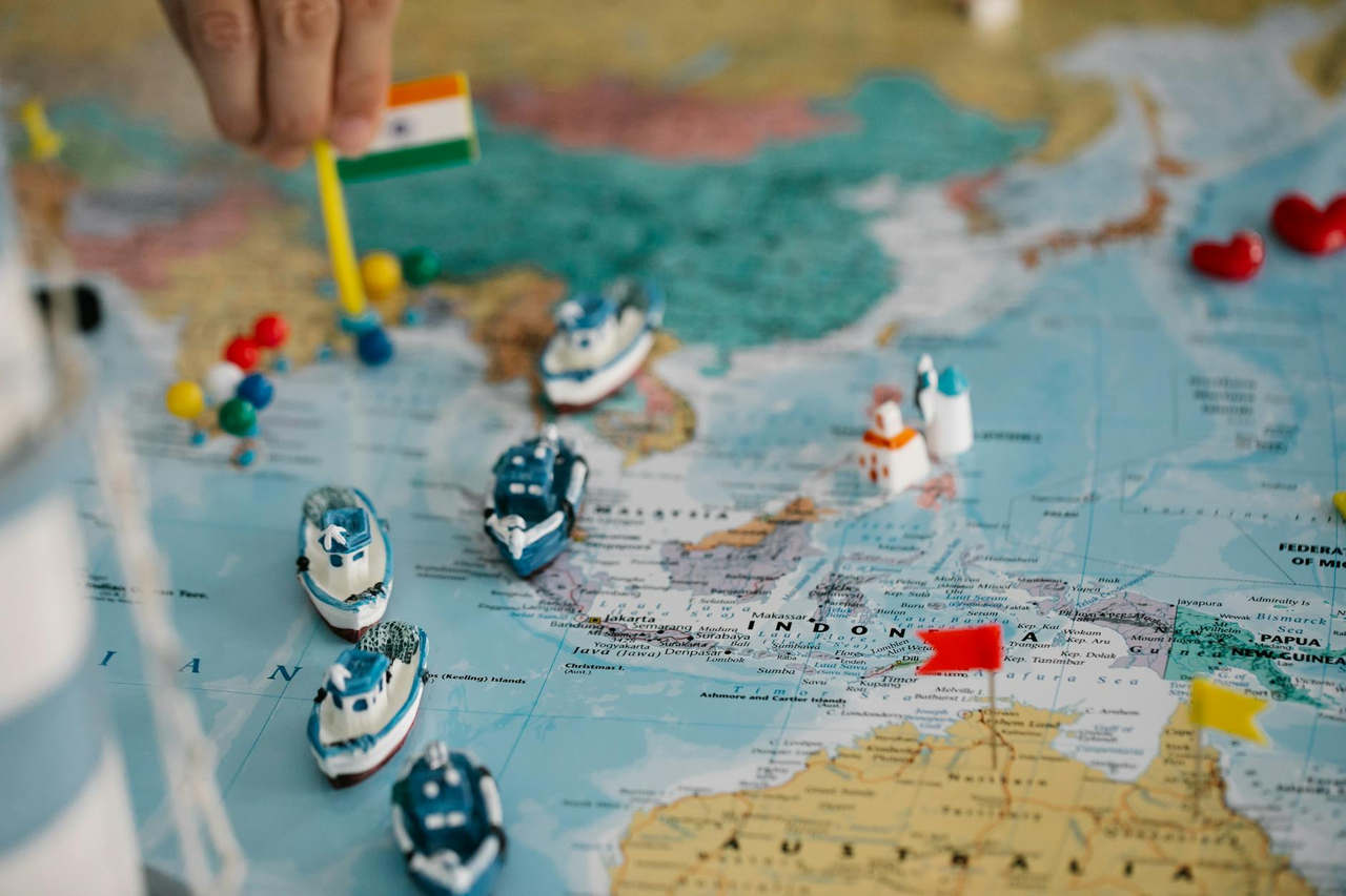 A detailed view of a world map with tiny model ships and flags indicating locations, highlighting global trade routes.