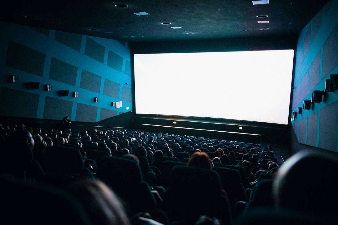 A crowded cinema audience seated in a theater watching a movie on a large screen.